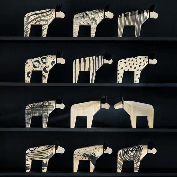 Twelve HÖSTAGILLE moose decorations are sitting on display shelves, three on each shelf. Some are partly painted black.