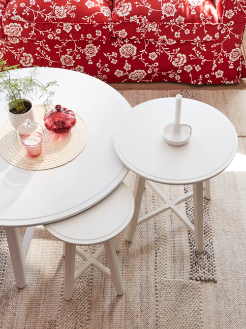 A round coffee table, a nest of two, round tables, a three-seat sofa, a red vase, and a low pile rug.