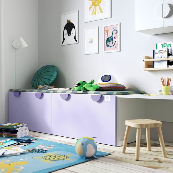 Corner of child's bedroom with purple SMASTAD drawers also acting as a bench. A rug is laid on the floor with a AFTONSPARV globe plush tool next to a FLISAT child stool. 