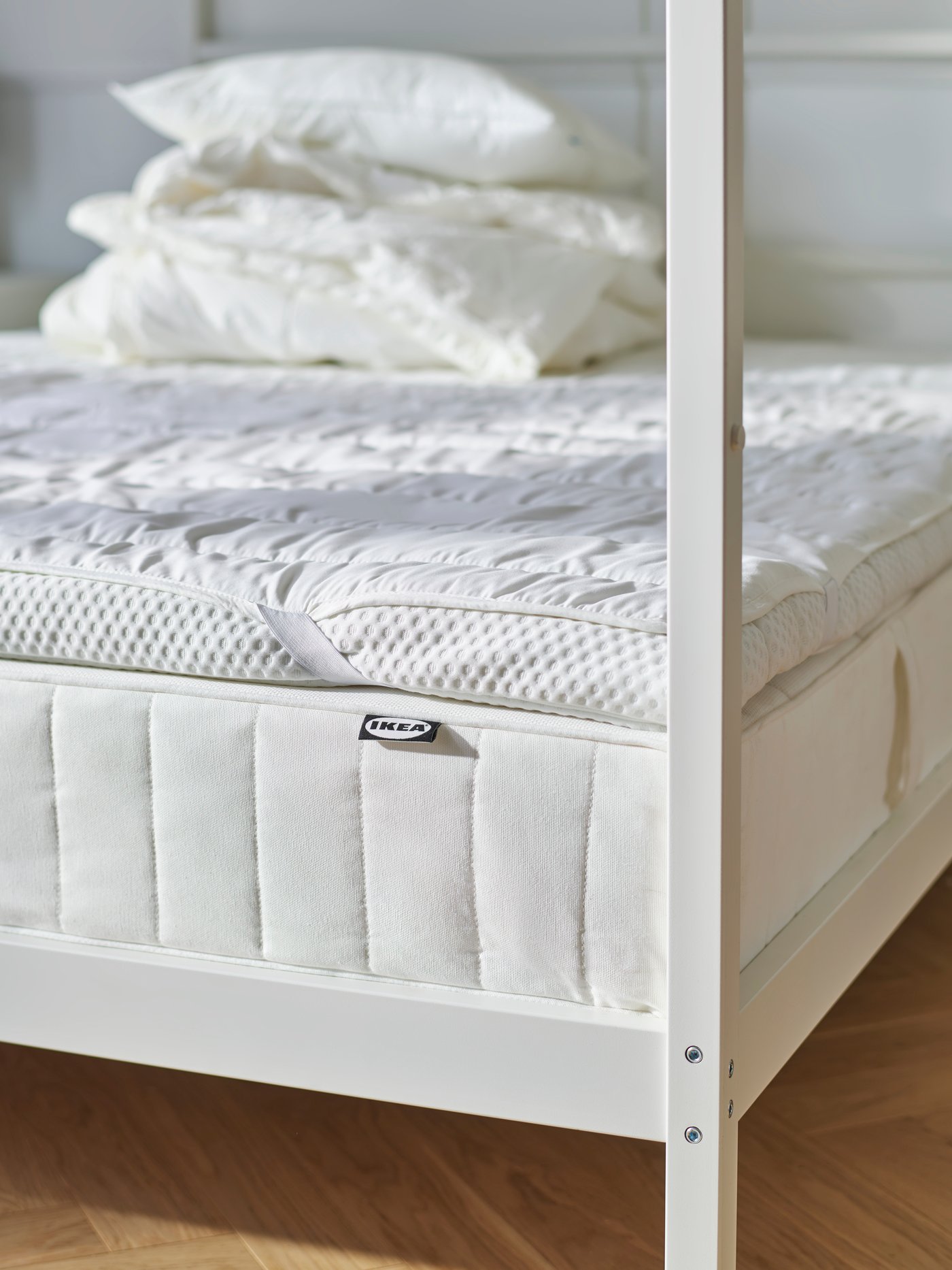 VITARNA four-poster bed with the different layers of mattresses visible, and a pile of duvets and pillows on top of it all.