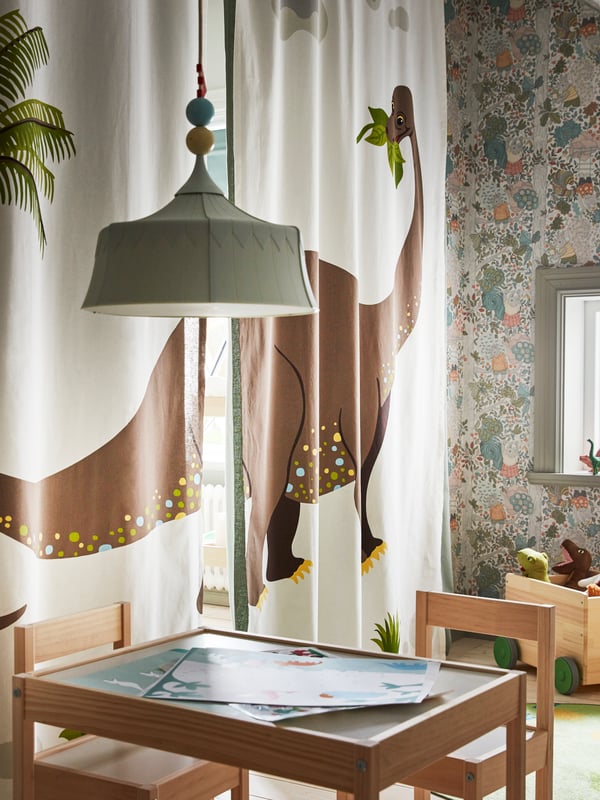 JÄTTELIK curtains with a LÄTT children’s table and chairs in front, and a TROLLBO pendant lamp hanging over the table.