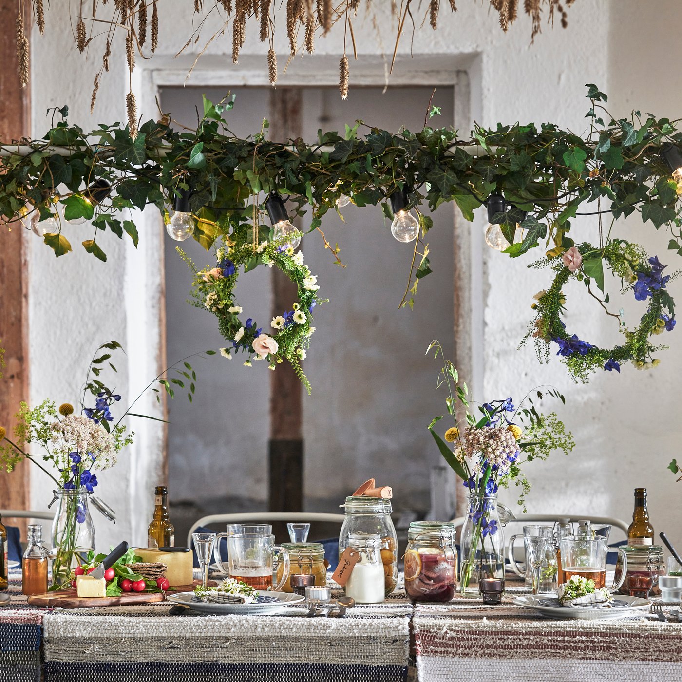 A long wooden table, festively decorated with garlands and floral wreaths. Food, drinks and a black IKEA RÅSKOG serving trolley are visible. A rustic atmosphere.