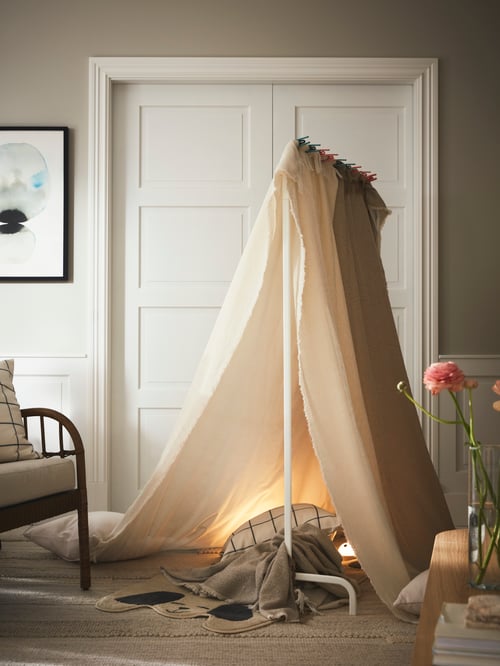 Living room area featuring a clothes rack propping up a beige throw akin to a tent, a white door, and an armchair.