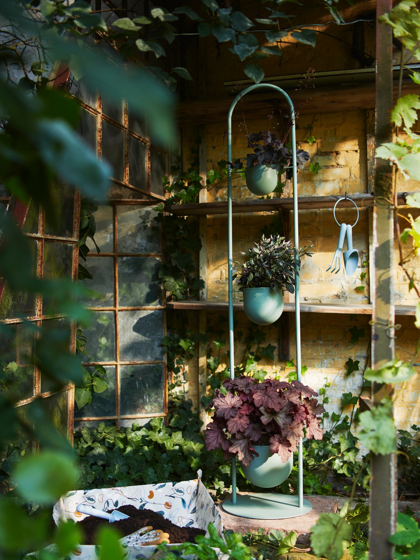 A lush, partially sunny garden corner with a light grey-green DAKSJUS plant stand with three plant pots placed vertically.