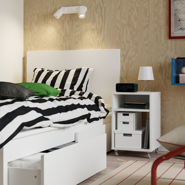 A white MALM bed frame with two storage boxes, one opened with textiles. On top is a SLÅNHÖSTMAL duvet cover.