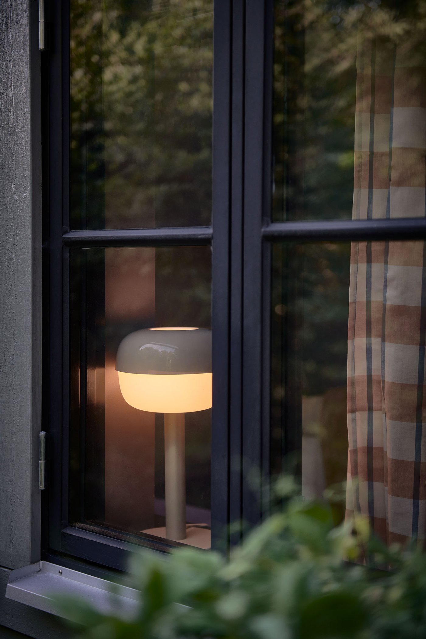 Bild tagen utifrån på en BLÅSVERK bordslampa som står i ett fönster.