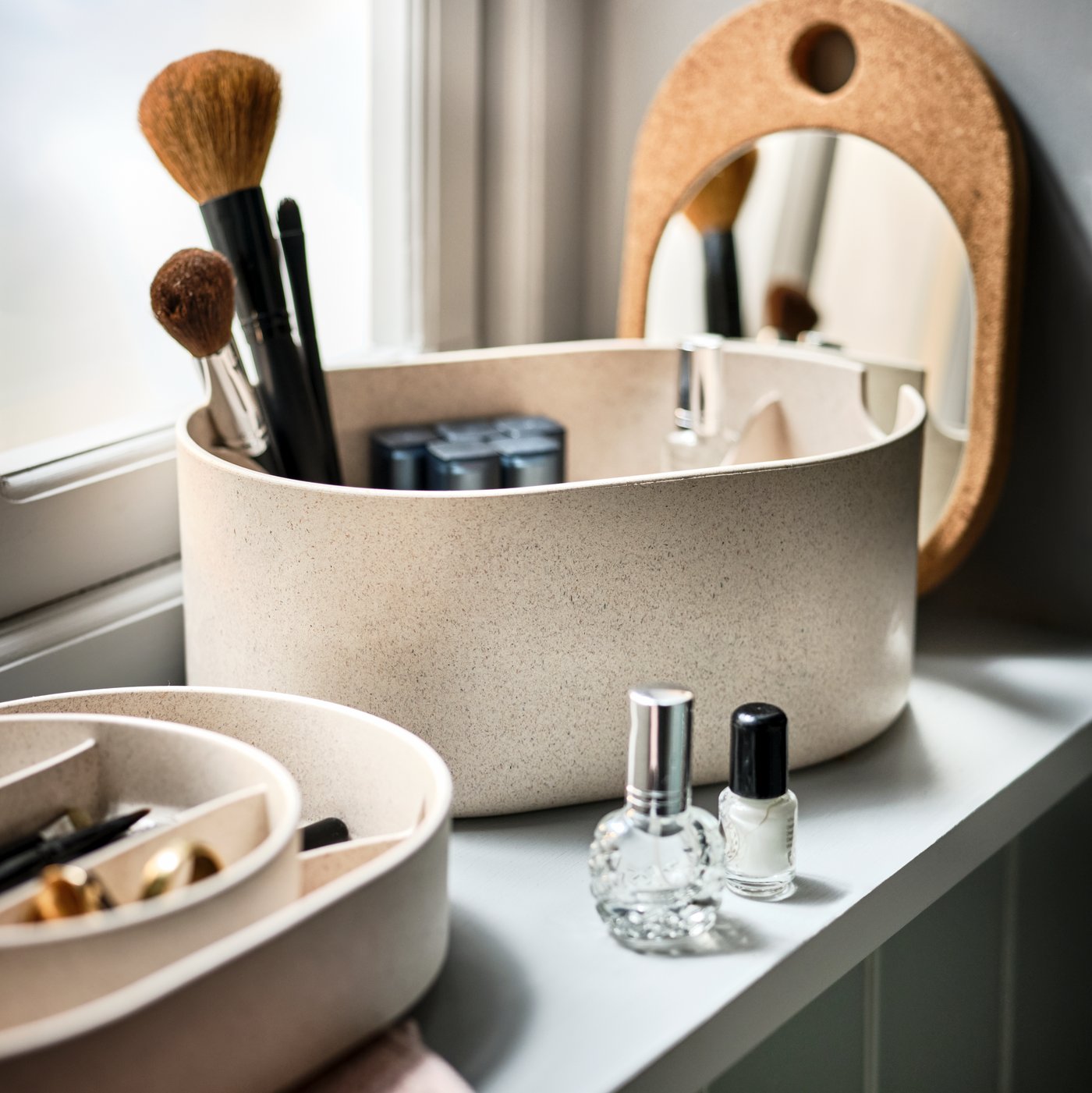 A windowsill in a bathroom holding a SAXBORGA storage box with mirror, filled with and surrounded by make-up accessories.