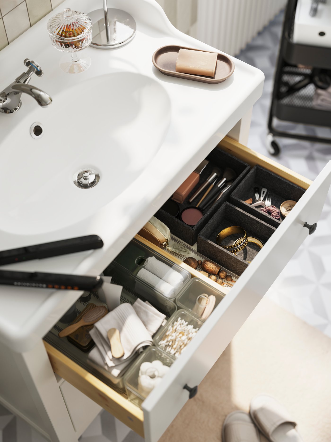 Un cajón abierto, colocado dentro de un mueble con un conjunto UPPDATERA de 3 cajas llenas de accesorios de baño, en un cuarto de baño.