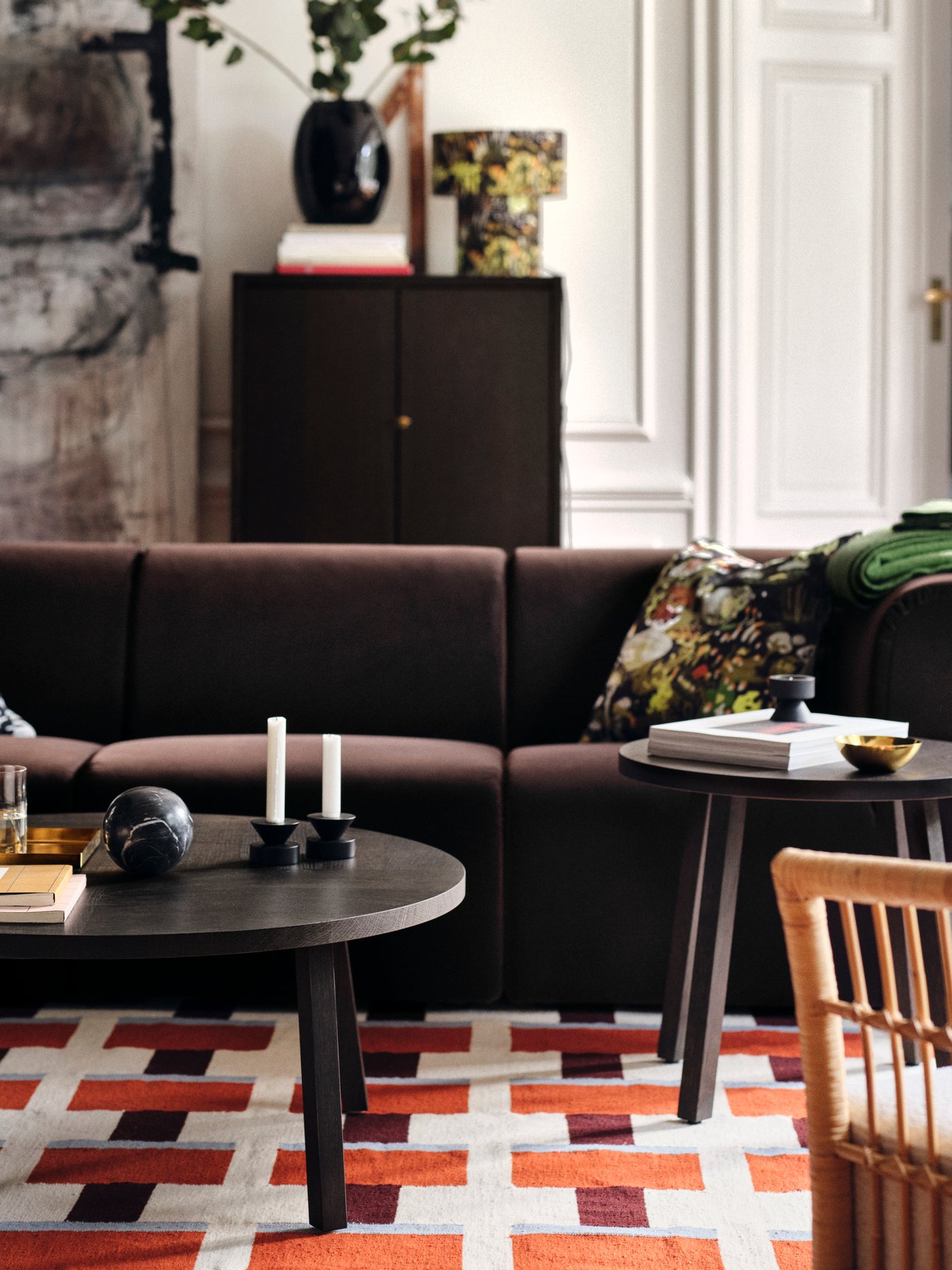 En brun soffa i ett vardagsrum med en mönstrad matta i rött och vitt.