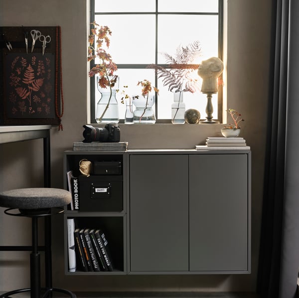 A dim room with a combination of dark-grey EKET cabinets mounted beneath a window. A WiFi speaker lamp is placed on top.