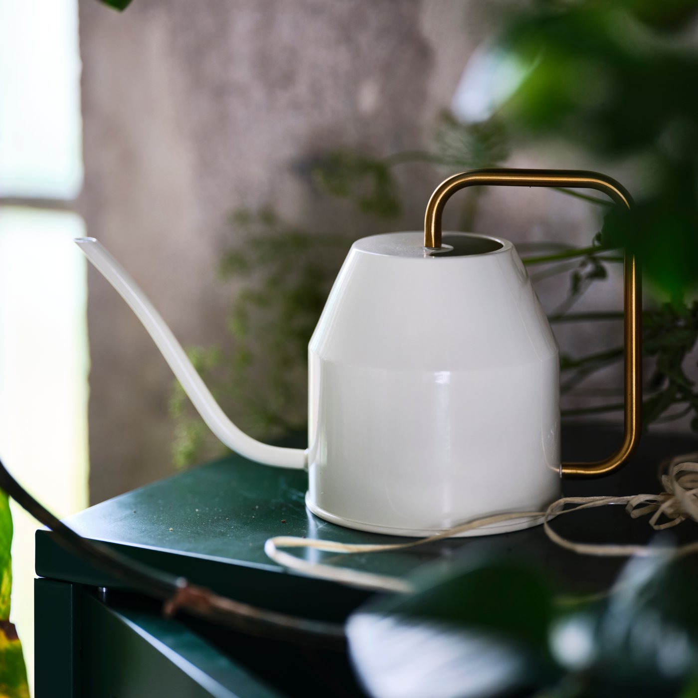 На улице стоит лейка VATTENKRASSE цвета слоновой кости/золотистого оттенка.