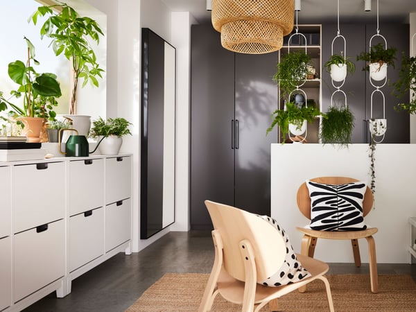 A hallway with dark grey PAX wardrobes, SINNERLIG bamboo lamp and STÄLL shoe cabinets underneath a windowsill with plants.