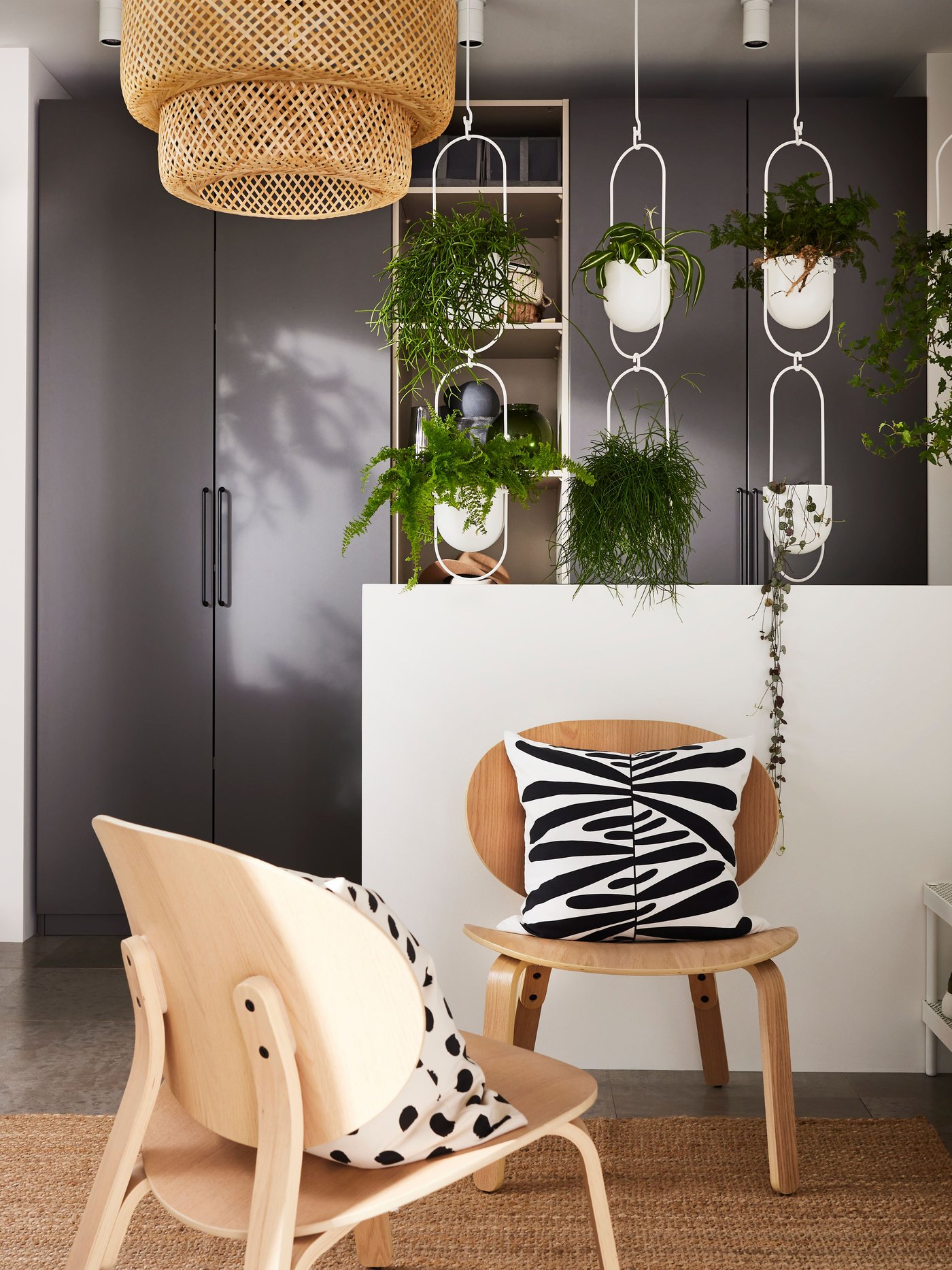 A hallway with dark grey PAX wardrobes, SINNERLIG bamboo lamp and STÄLL shoe cabinets underneath a windowsill with plants.