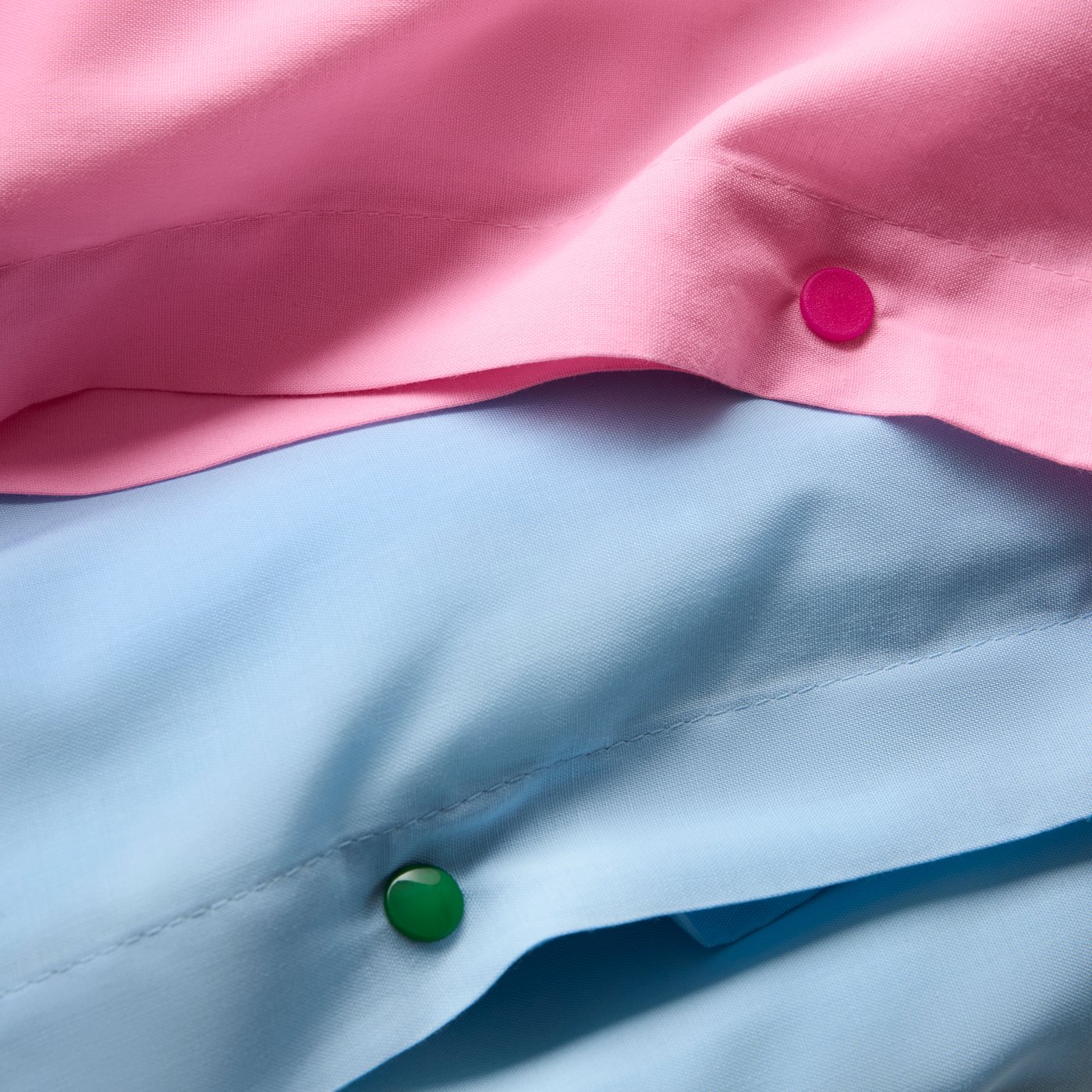 Close-up of two PILTANDVINGE pillow cases, one in pink with a pink button and one in blue with a blue button.