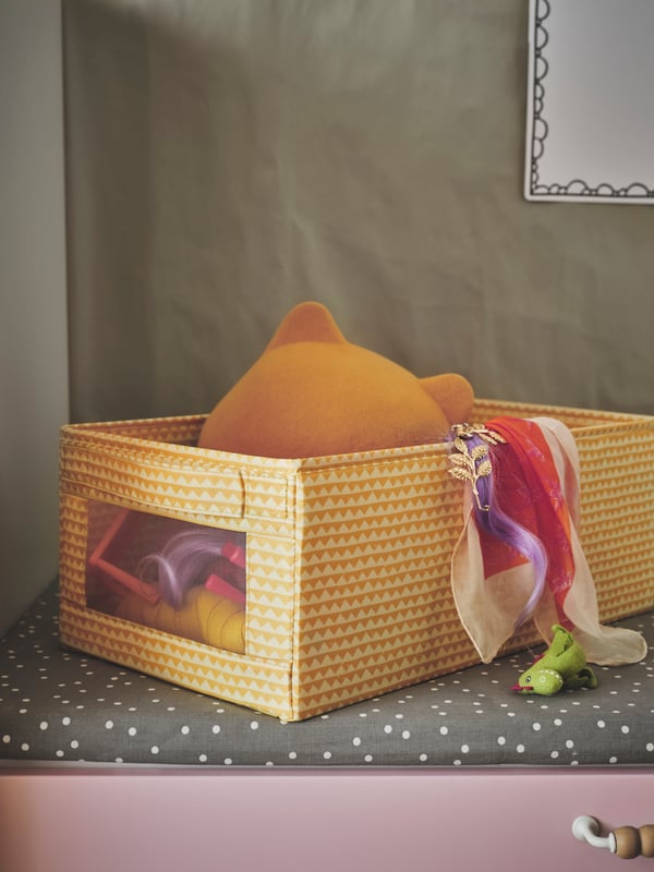 A yellow UPPRYMD box filled with toys, placed on a grey BÄNKKAMRAT bench pad with a pink drawer beneath.