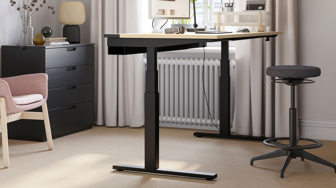 A home workspace featuring an electric MITTZON sit/stand desk in birch veneer/black, paired with a black stool.