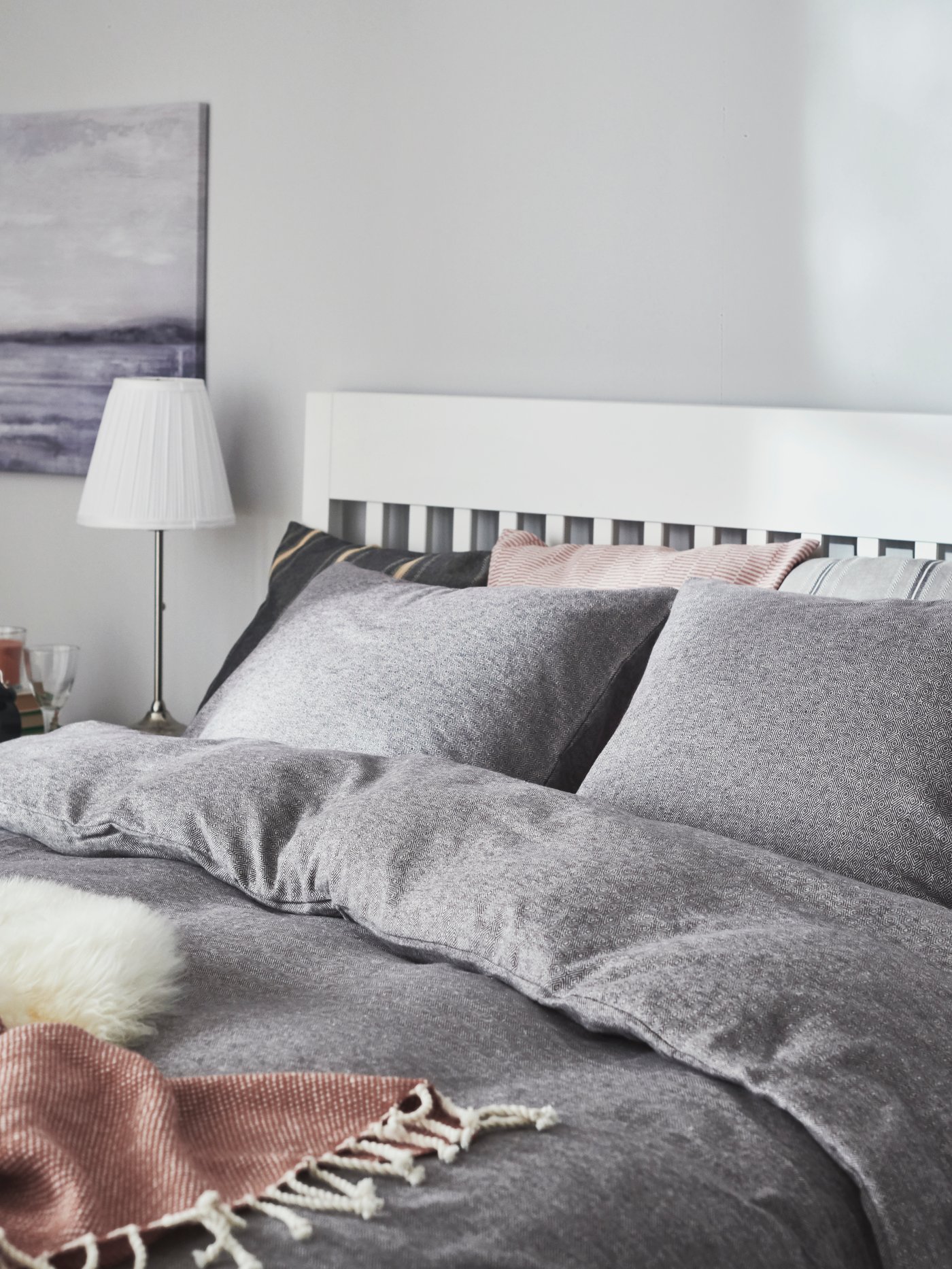 Schmales, gemütliches Bett mit blauer Bettwäsche und hellem Bettlaken. Davor steht ein kleiner grauer Beistelltisch.