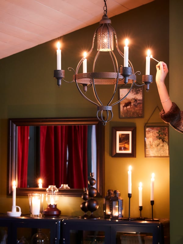 A black, traditional ÄPPELVIKEN pendant lamp with three lit decoration bulbs hanging next to an armchair and a coffee table.