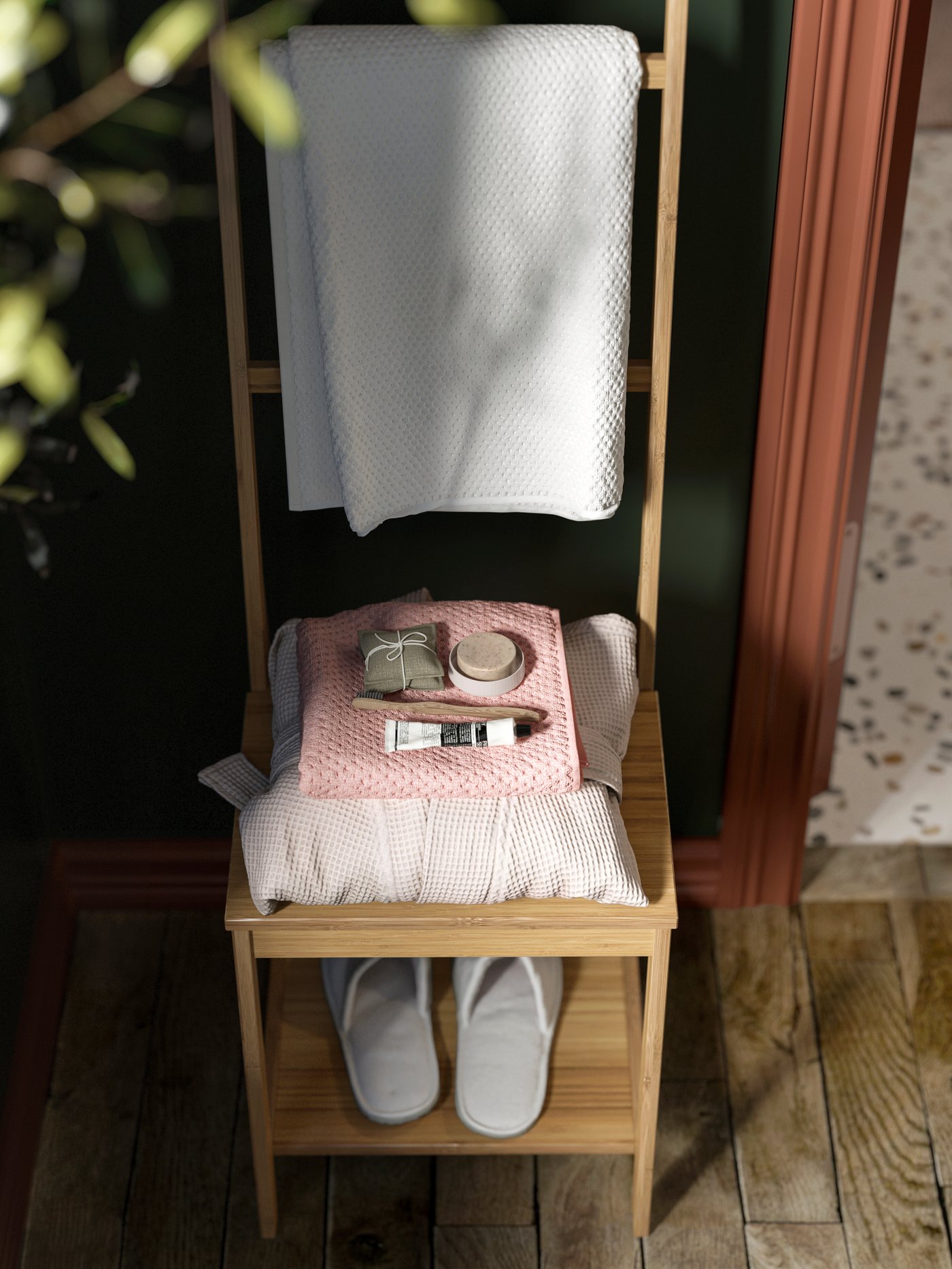 En RÅGRUND handdukstorkstol med snyggt staplade handdukar, badartiklar på en rosa trasa och tofflor på den nedre hyllan.