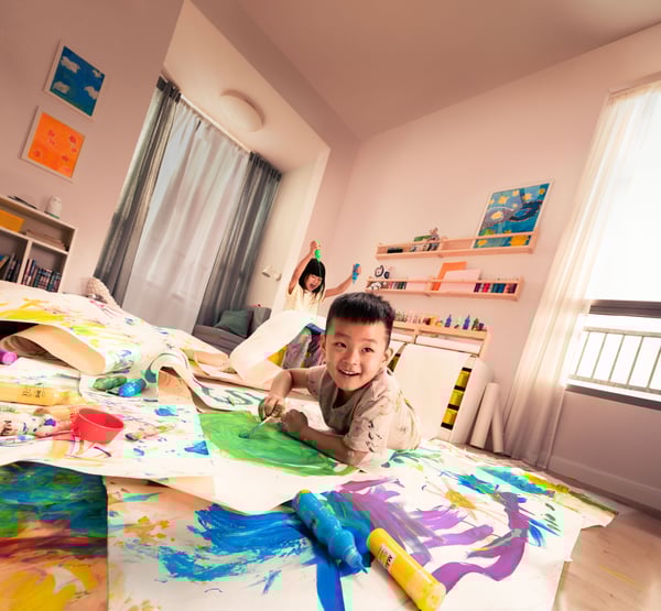 Two children playing in a room, painting with various colours on paper rolls on the floor