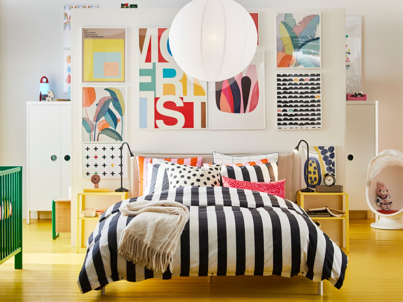 Furnished bedroom with yellow floor with the bed in the middle and a large picture wall behind.