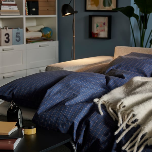 A softly lit living room with a BÅRSLÖV sofa-bed made with DOFTAKLEJA bed linen and an OLSERÖD side table by the bed.