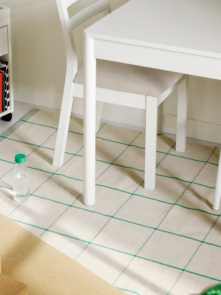白いチェアの下に敷かれているオフホワイトにグリーンの線が入ったRIDSTIG/リードスティグ ラグ。