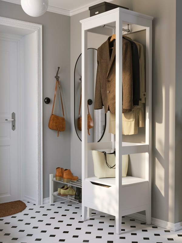 In a hallway with a black-and-white-patterned floor stands a white IDANÄS open wardrobe, a few jackets on hangers in it.