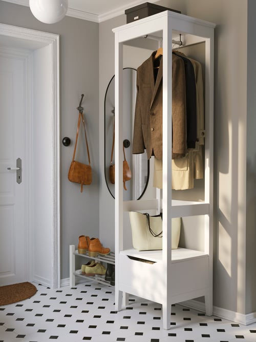 Hallway with an open wardrobe with clothes, a storage box on top, a mirror on the wall, and a shoe rack on the floor.