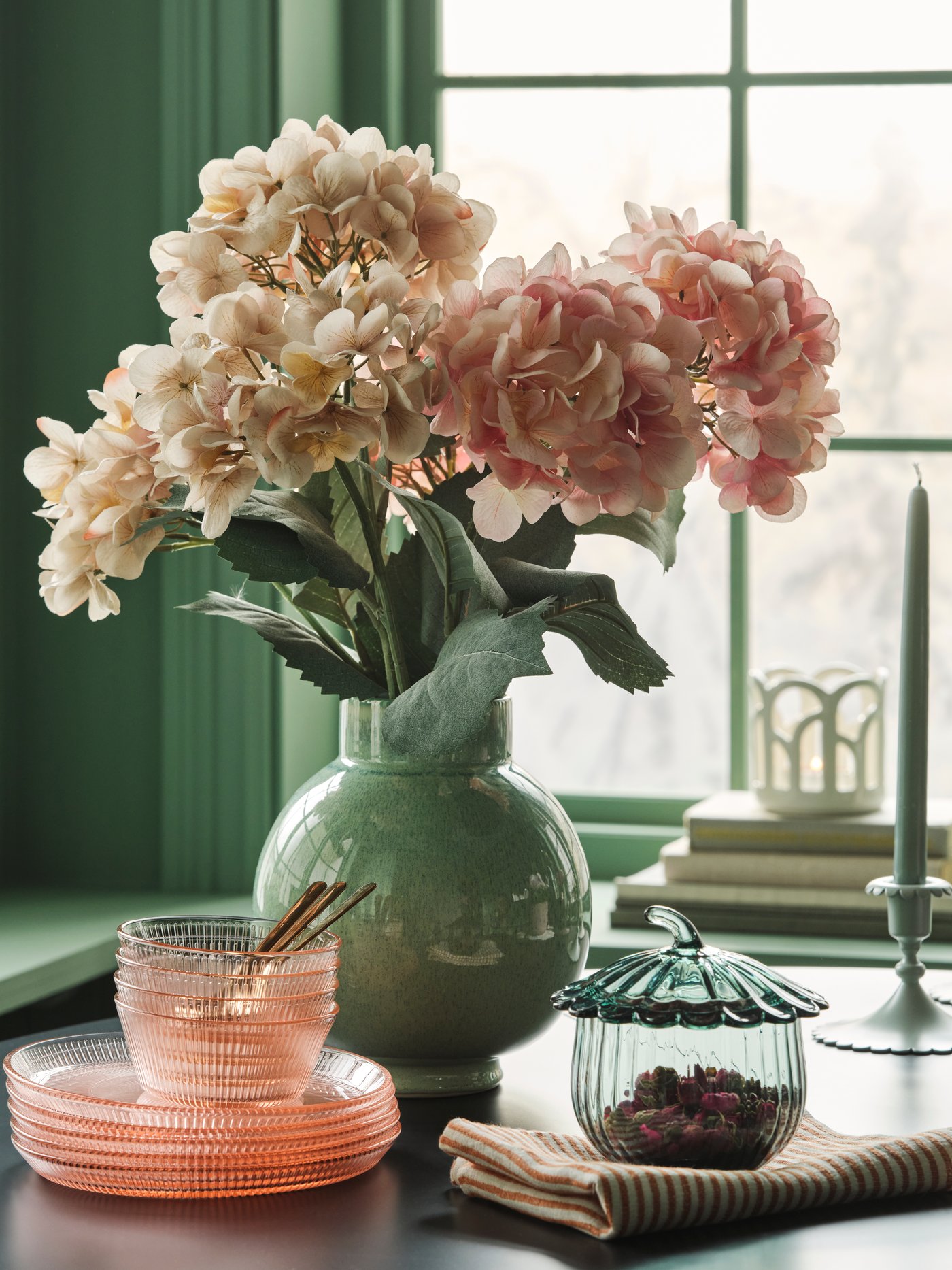 A bouquet de SMYCKA artificial flower in light pink and beix estand in green vase on table with glass plats and bowls.