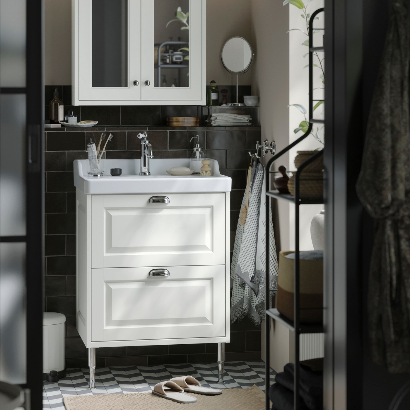 A small traditional style bathroom with white TÄNNFORSEN storage furniture, two soft round lamps and black details.