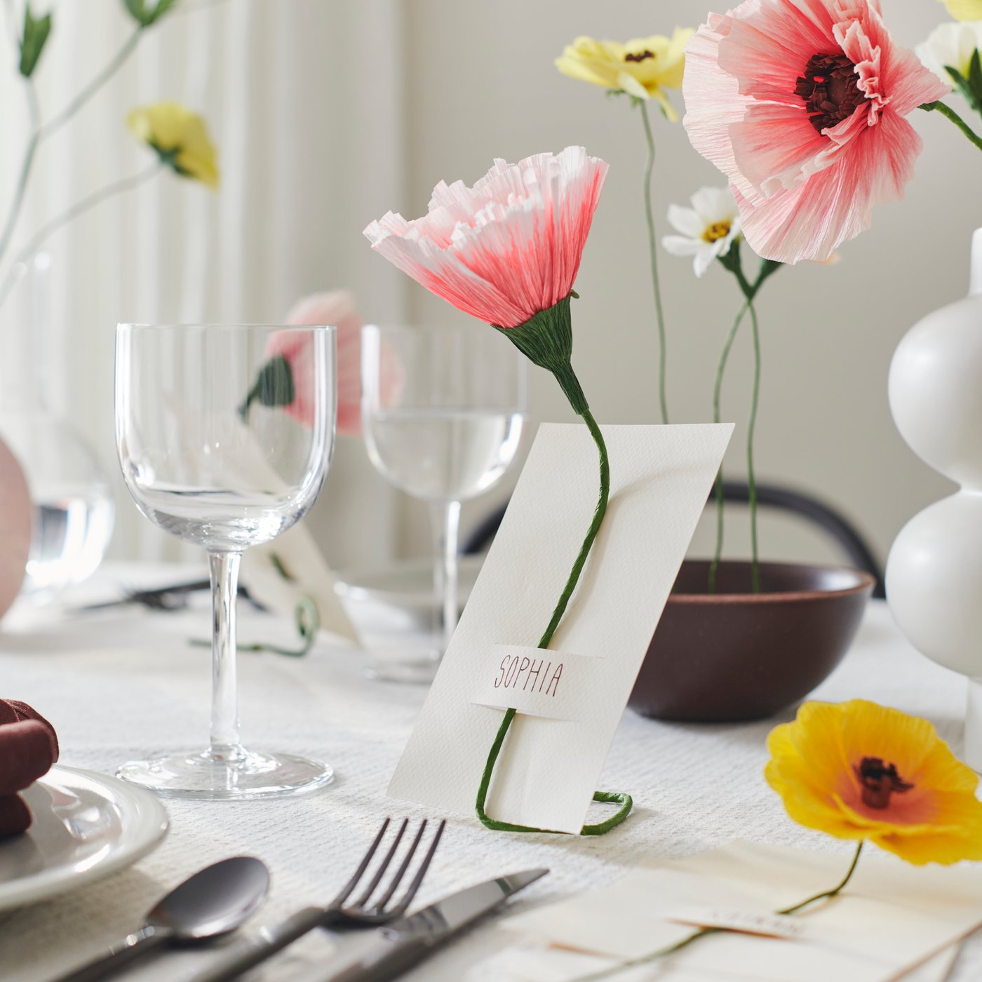A table is decorated for a party with GULDSPETT artificial flowers, including placement cards with flowers attached to them.