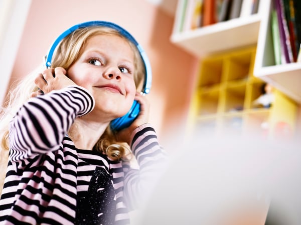 Young, blonde girl holding blue headphones over her head