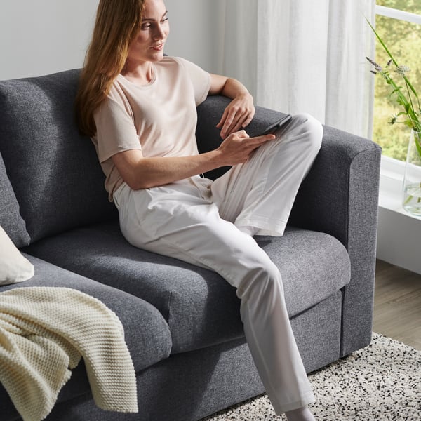 A woman sits on a dark grey couch, holding her mobile phone.