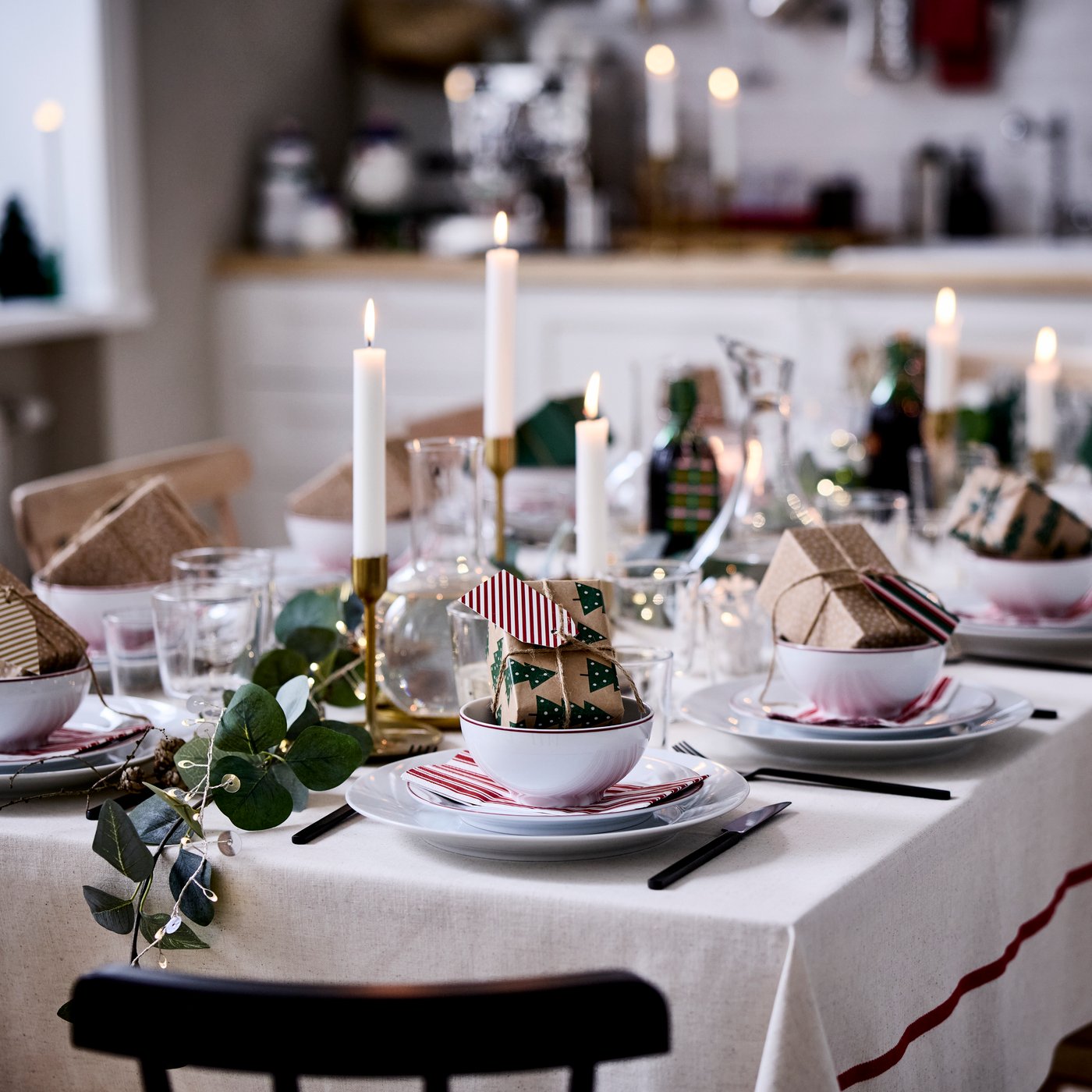 Une table de Noël chaleureuse est dressée avec des décorations VINTERFINT, des bougies allumées et de petits cadeaux emballés dans des bols.