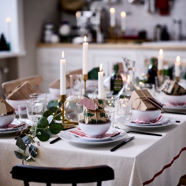Ett mysigt julbord dukas med VINTERFINT-dekorationer, tända ljus och små inslagna presenter i skålar.