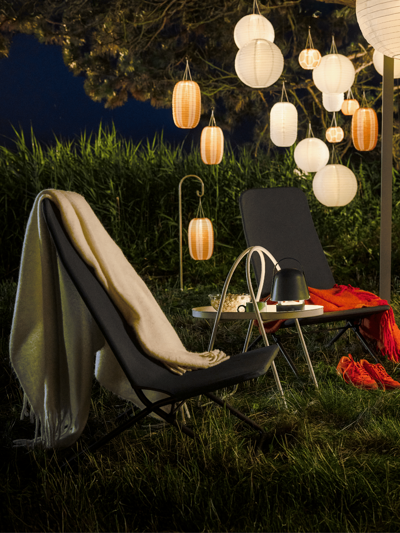 A cosy evening garden area with hanging lights features a dark grey VIGGSÖ lounge chair, surrounded by greenery.