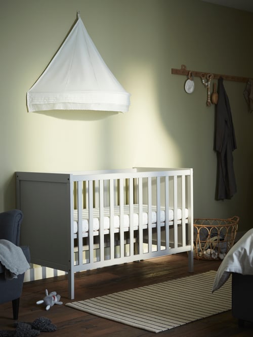 Minimalistisches Kinderzimmer mit einem SUNDVIK Babybett, einem LEN Betthimmel und einer HÖVOLM Leiste mit 6 Haken.