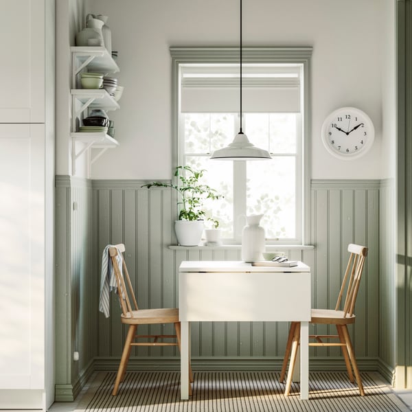 A HAUGA drop-leaf table in white and birch veneer and two HÖGVED chairs in birch veneer are placed next to a window.