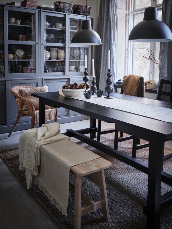 A NORDVIKEN dining table with a bench and various chairs around it. Candlesticks are on top and two pendant lamps are above.