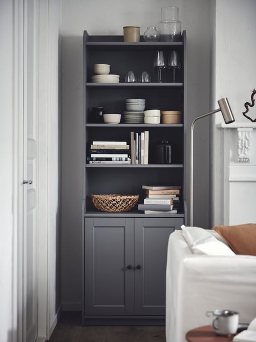 A living room featuring a grey high cabinet with 2 doors with both open and closed storage next to a grey floor reading lamp.