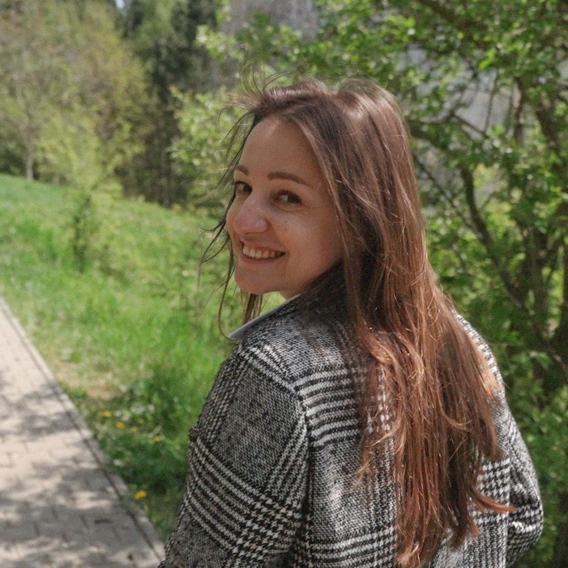 Nataliia, smiling brightly, walks along a picturesque path surrounded by lush greenery.
