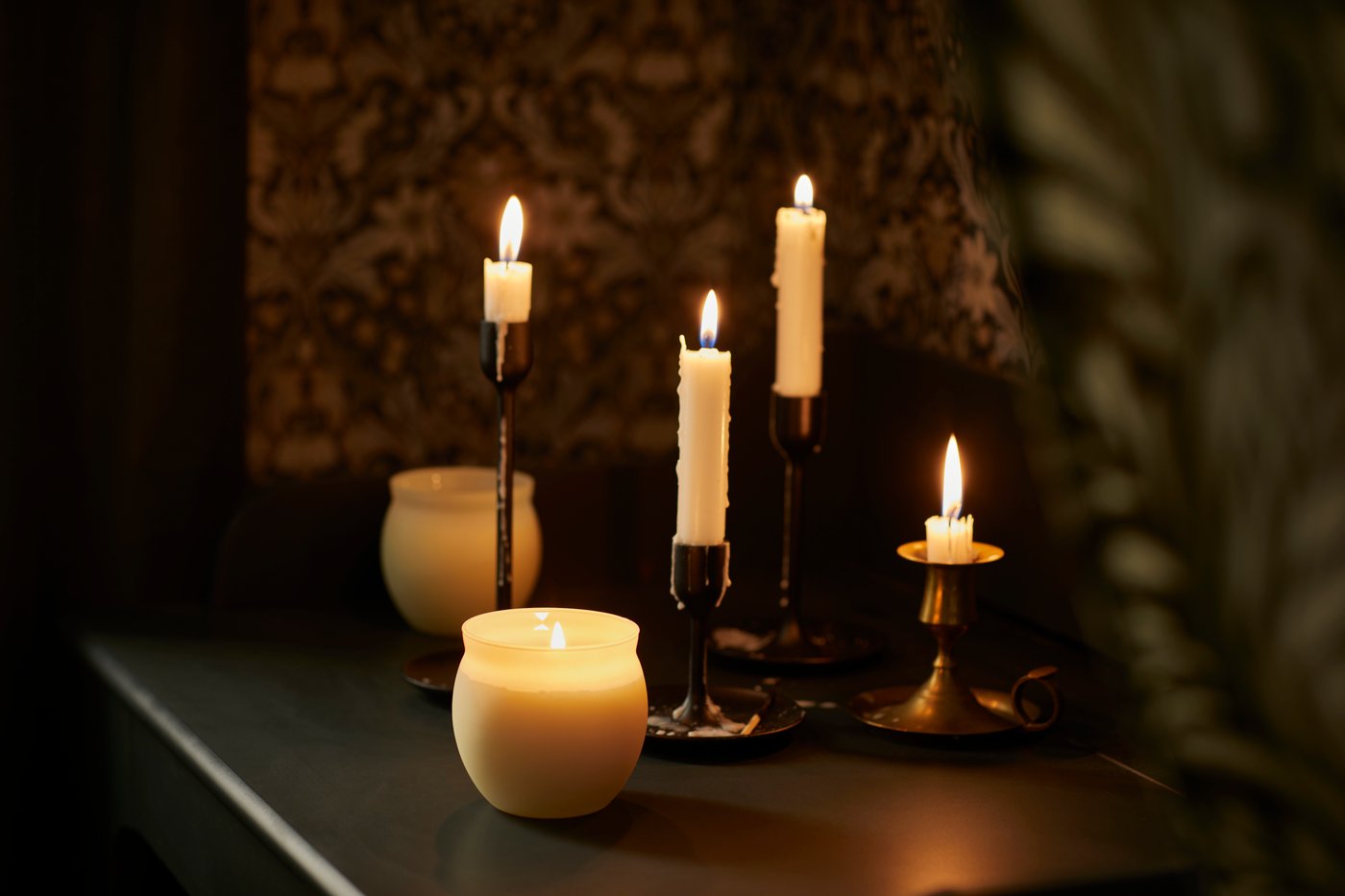 Four lit white dinner candles in gold candlesticks next to two scented candles in white glass holders.