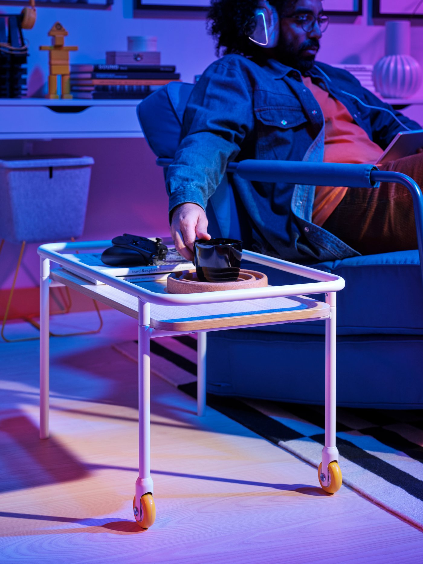 Eine Person greift nach einem Becher, der auf einem BRÄNNBOLL Beistelltisch mit Rollen steht.