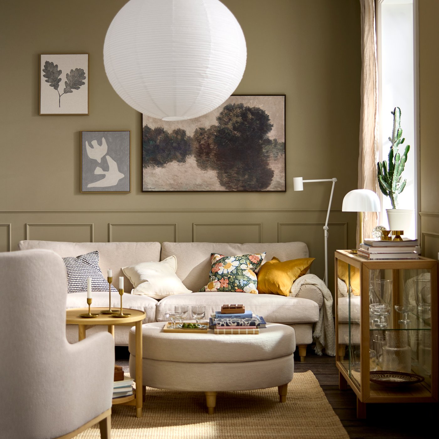 A living room with a light-beige VALNÄS sofa dotted with colourful cushions, a round VALNÄS footstool acting as coffee table.