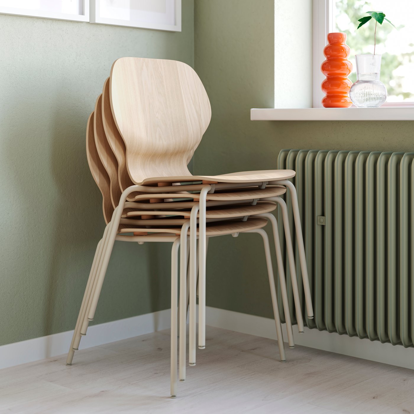 Stacked light wood chairs with metal legs beside a radiator and window with decorative vases.
