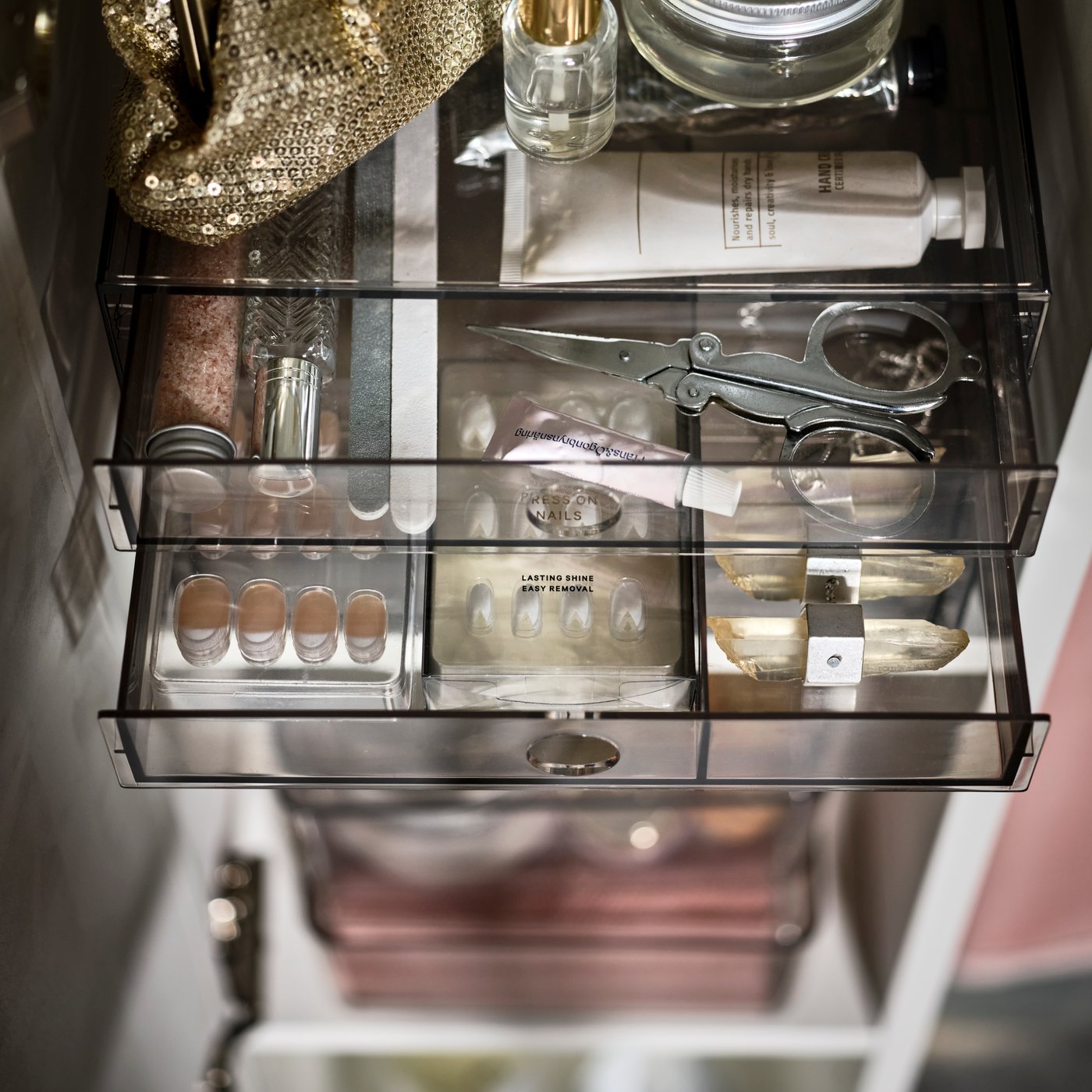 A narrow cabinet with its shelves filled with beauty paraphernalia, some of it in a smoked-plastic GODMORGON mini chest.