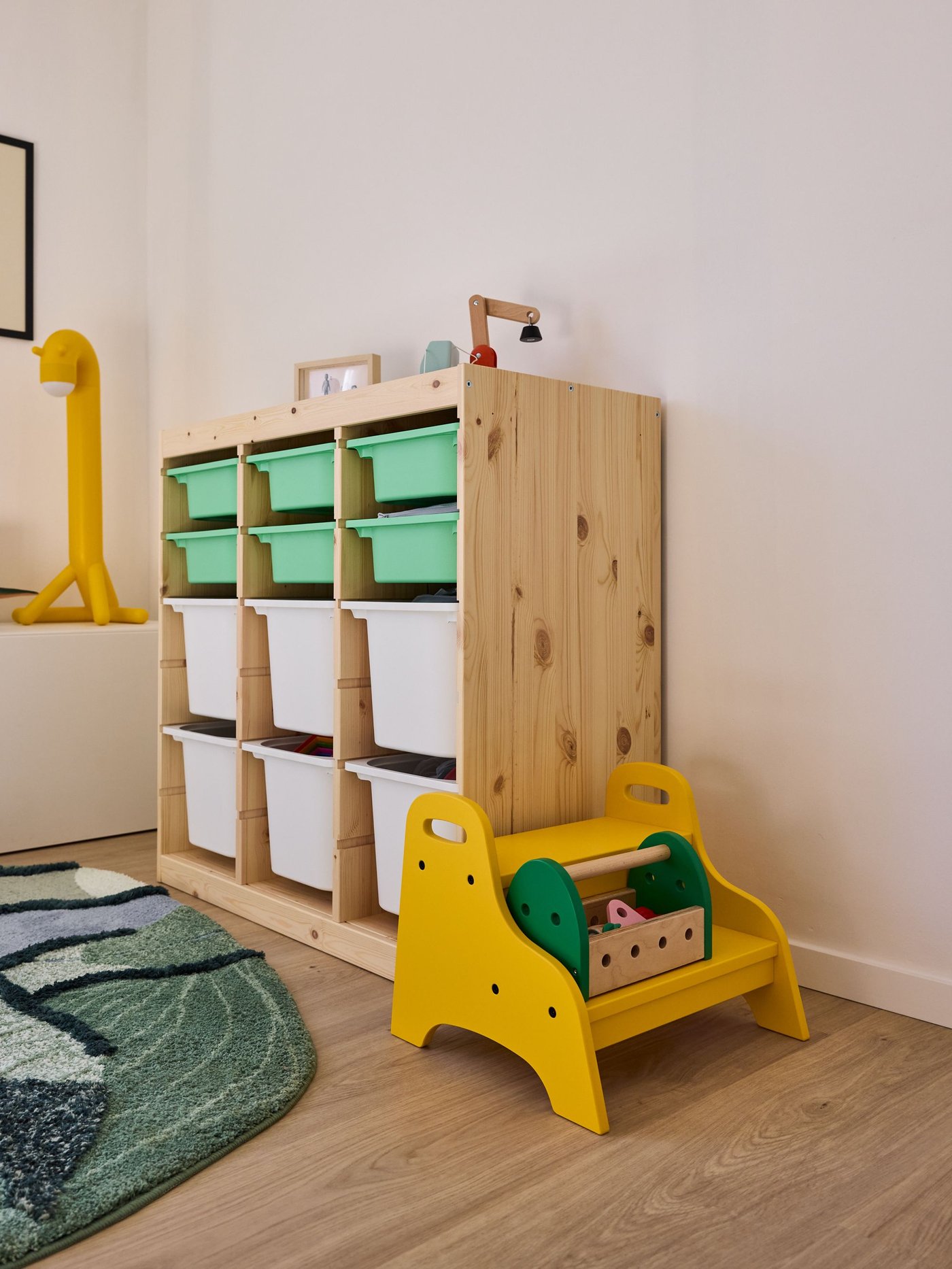Houten opbergkast met bakken en geel kinderstoeltje in speelhoek, opgeruimde en warme uitstraling.