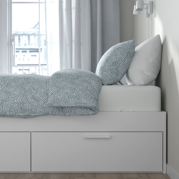 Una cama BRIMNES blanca con ropa de cama en tonos celestes con blanco.