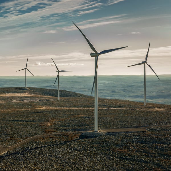 Several wind turbines stand tall on a hilly landscape, harnessing the power of the wind under a cloudy sky.